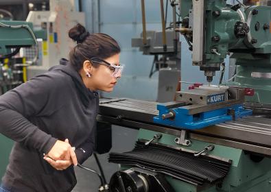A person in a black shirt and goggles standing next to a machine.