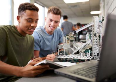 Two male students at desk with laptop and engineering model